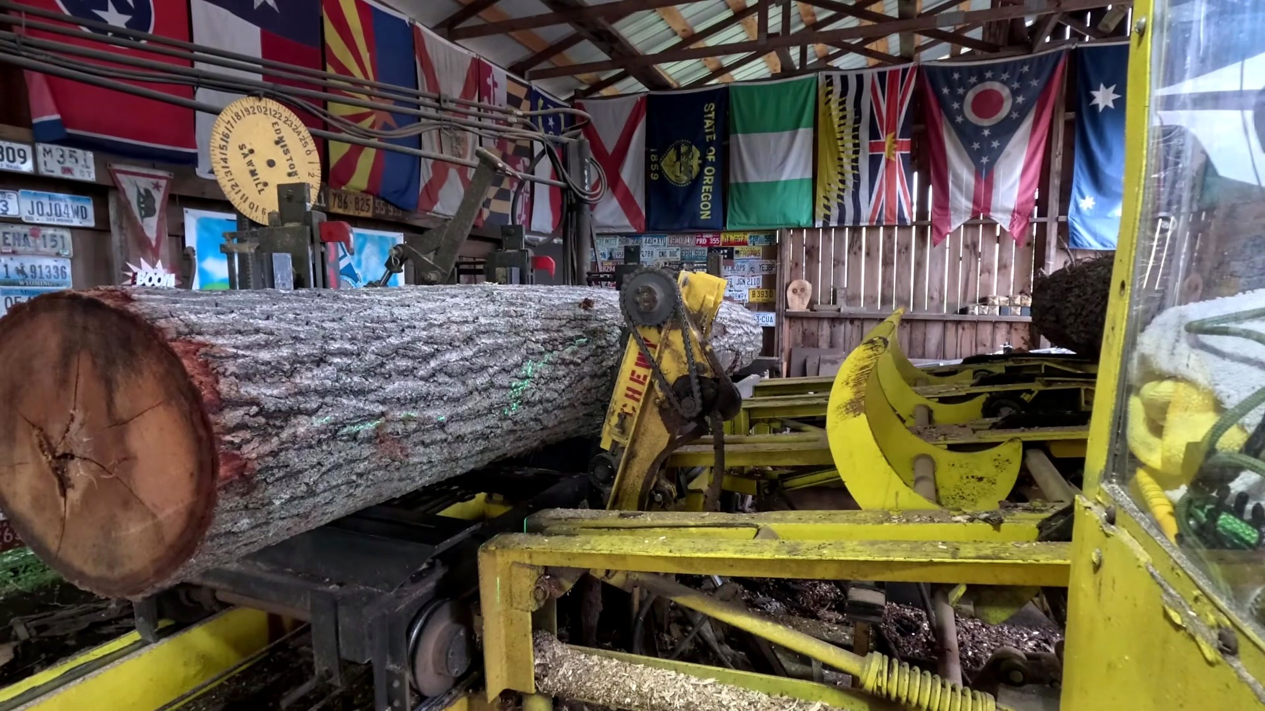 banana oak sawmill board cutting process - a bark-covered log supported on the sawmill carriage beside the loading mechanism