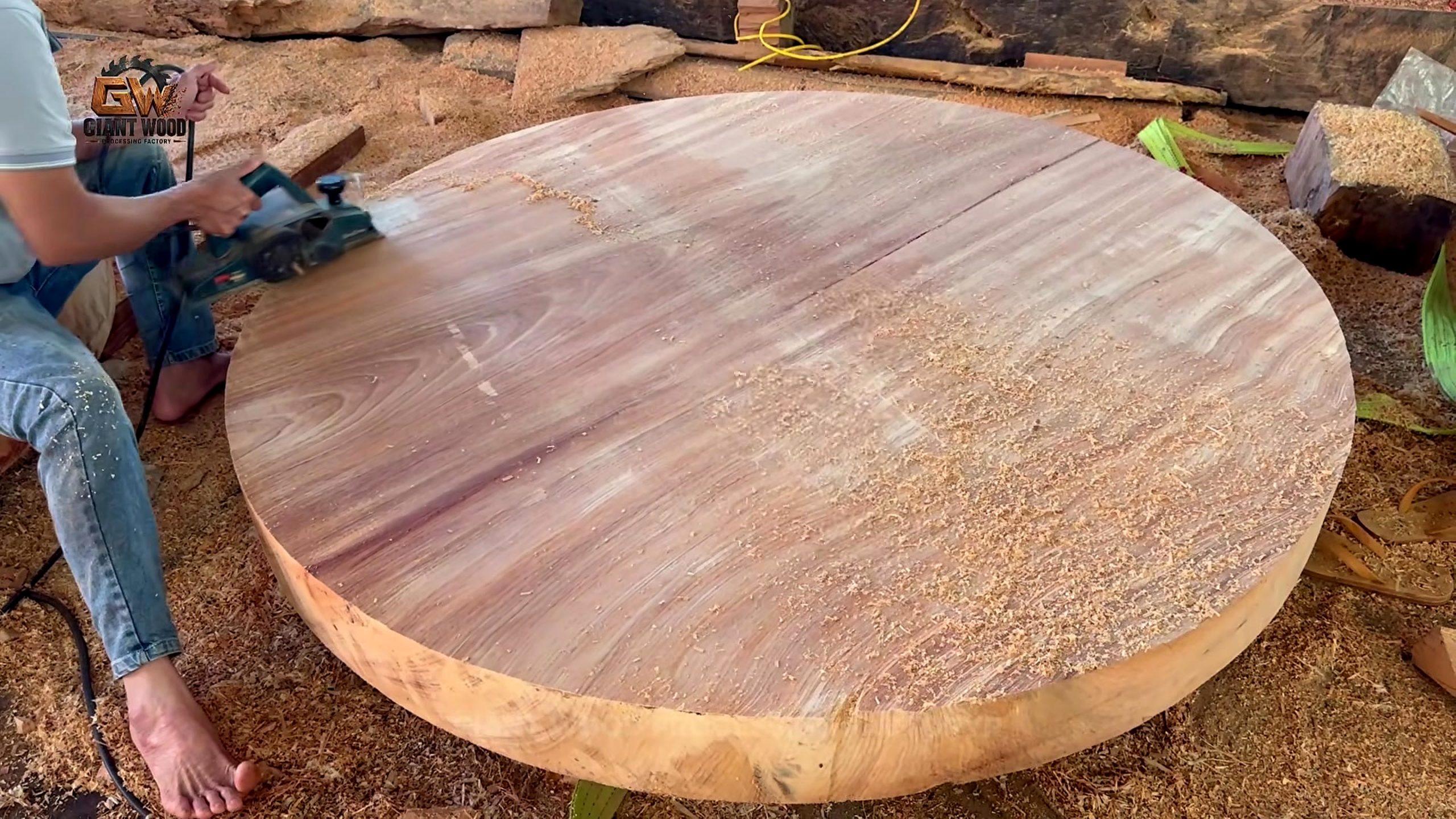 worker surfacing a thick round timber blank with a handheld electric tool