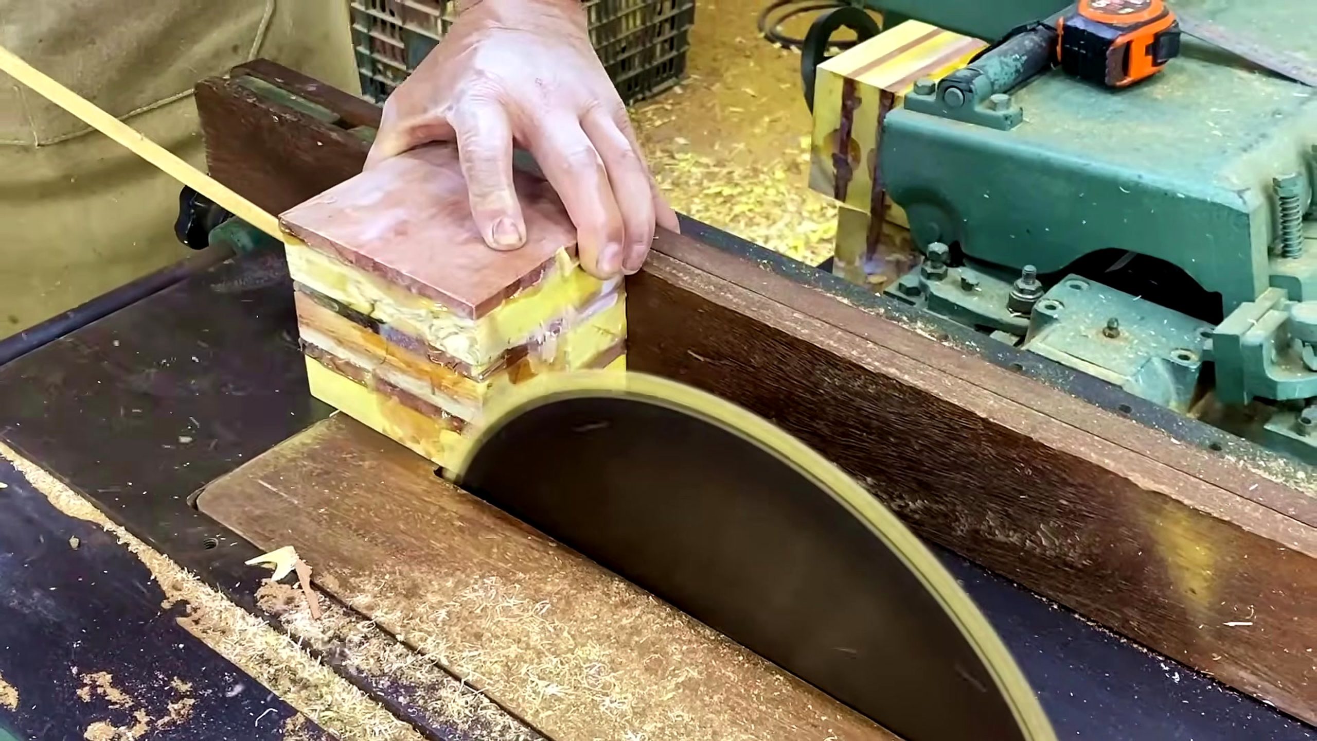 laminated wood disk turning process - a stacked colored wood block being trimmed against a table saw fence