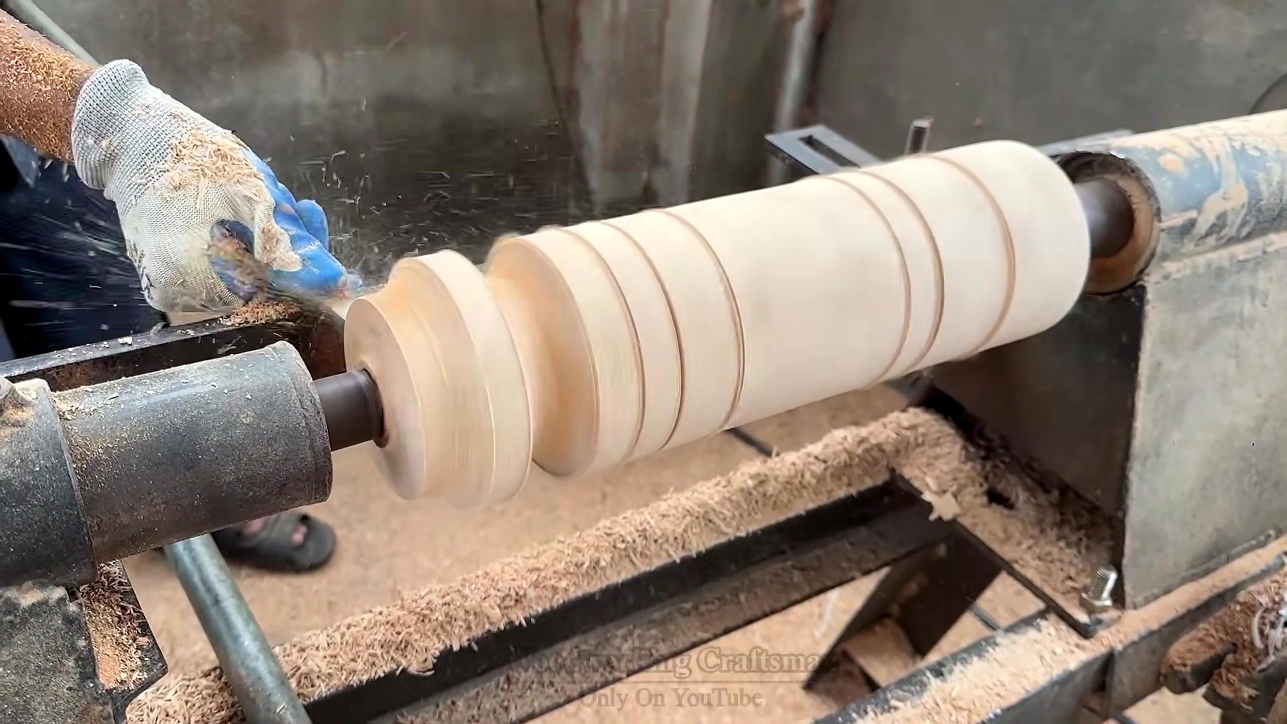 segmented round wood table making process - a lathe shaping repeated beads, coves, and shoulders on a support