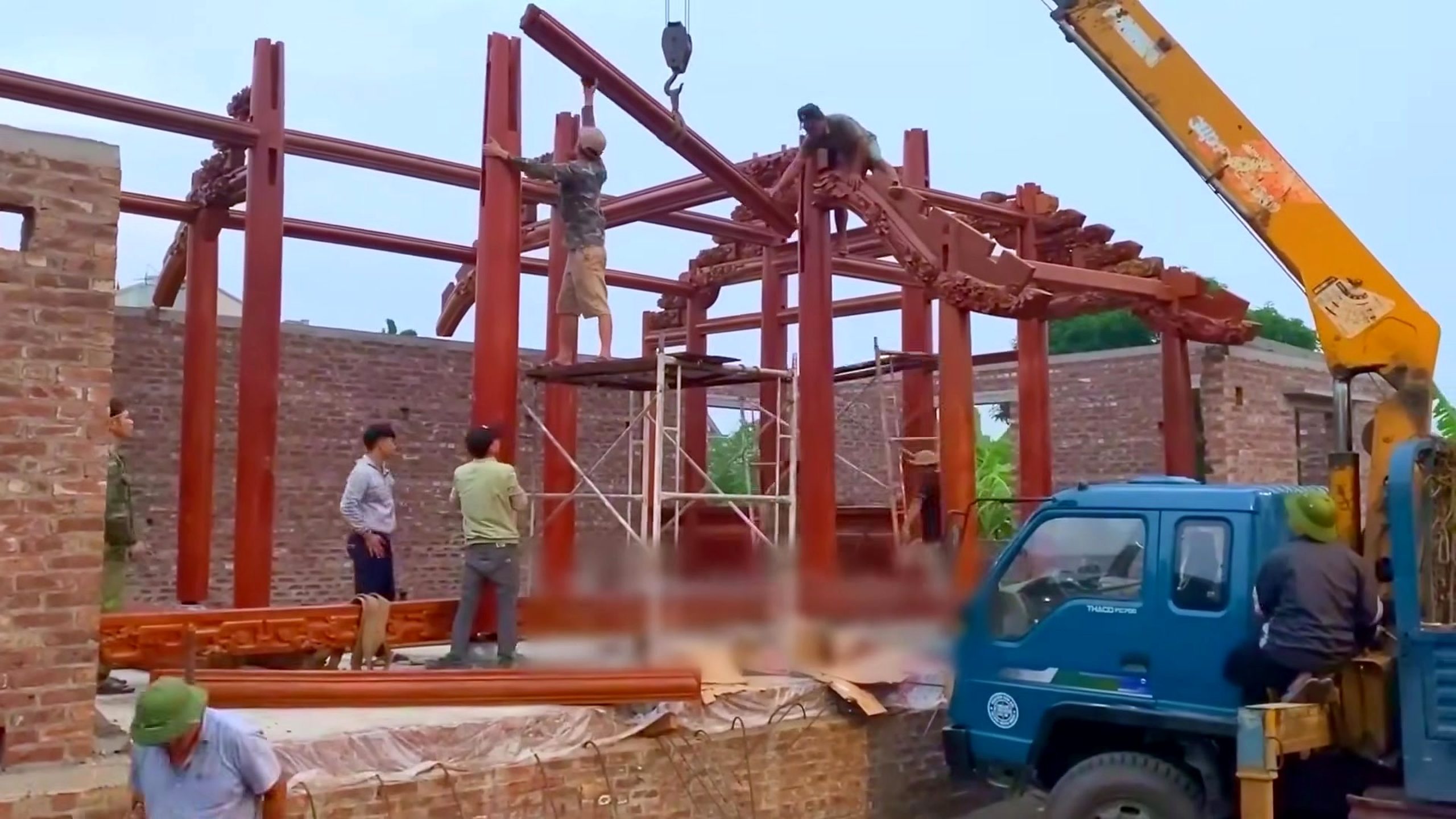 traditional timber frame mortise and tenon assembly - a crane supporting a heavy timber member as another structural bay is assembled
