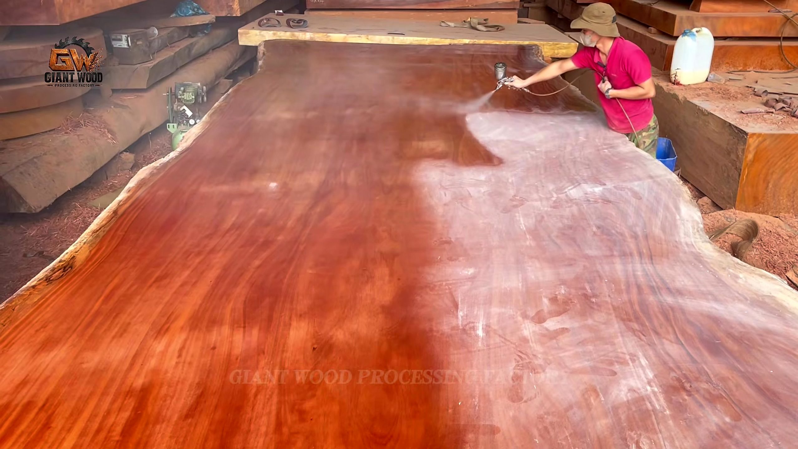 inside million wood factory giant log - liquid finish being spread over a reddish live-edge slab