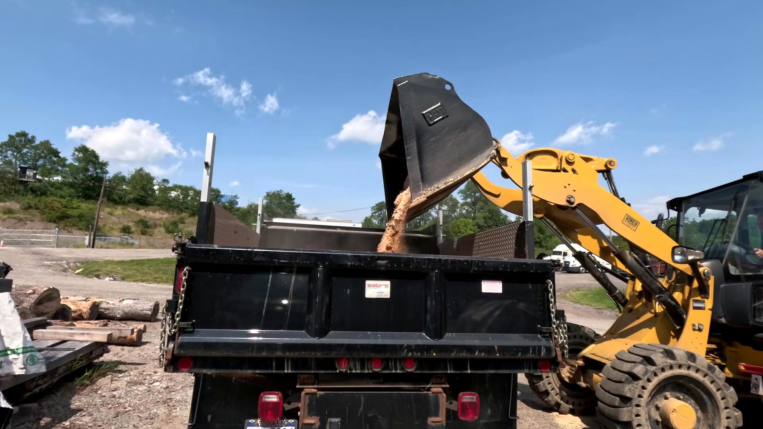 sawmill chop saw blade and log crosscut workflow - a wheel loader clearing loose sawmill residue into a dump body