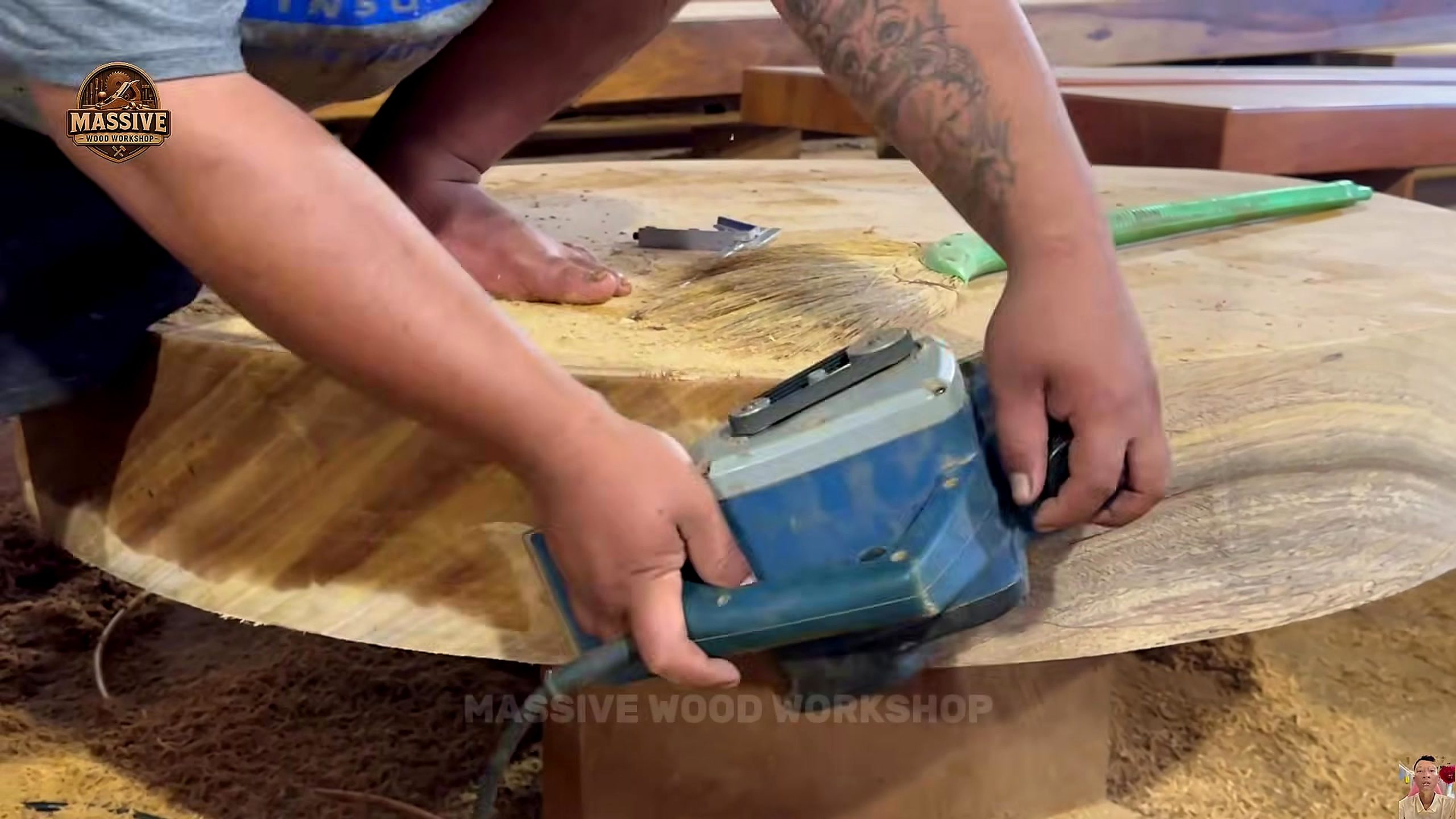 weathered giant timber round table process - a handheld sander working across the thick circular tabletop blank