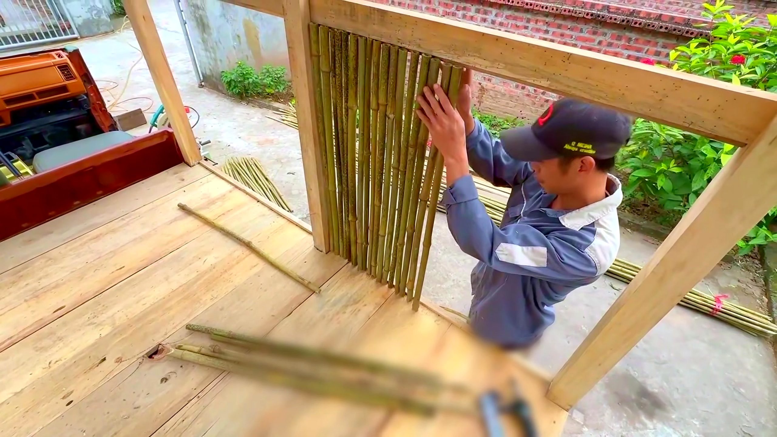wood and bamboo pavilion build with miter saw - vertical bamboo poles being fitted within a timber wall frame above the deck